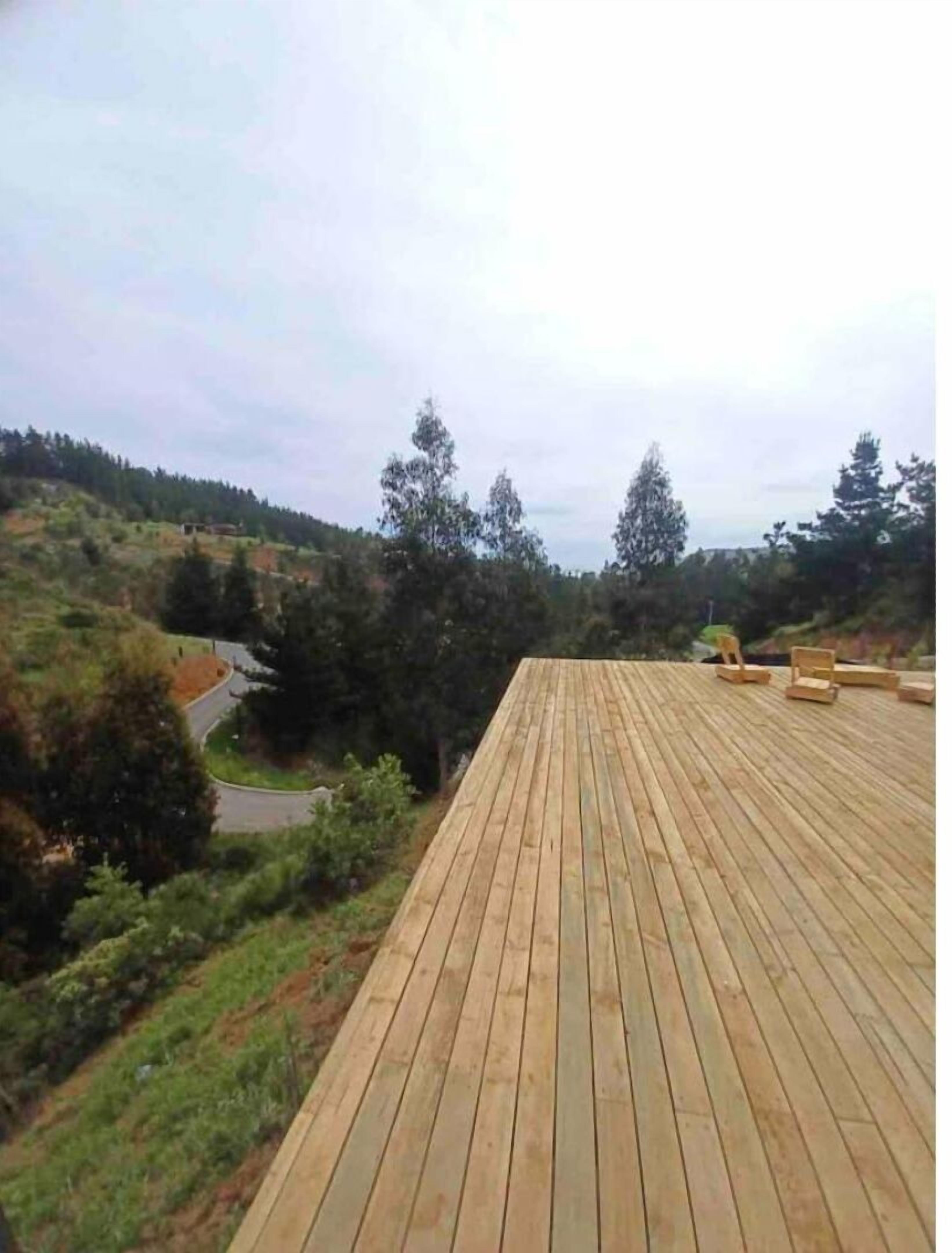 A wooden deck with a view of a hilly landscape and a road.