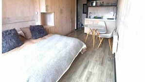 A compact bedroom with a bed, a desk, and a kitchenette. - Vista Mar Pupuya Matanzas Cabaña 2 (O'Higgins)