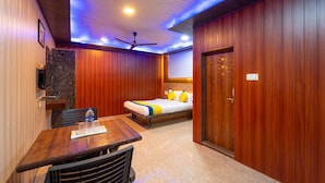 A hotel room with a wooden ceiling, a bed with yellow pillows, a wooden table with chairs, and a ceiling fan. - Itsy Hotels Sun N Shade (Karjat)