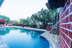 A swimming pool with a tiled edge, surrounded by a brick wall and a metal fence. - Itsy Hotels Sun N Shade (Karjat)