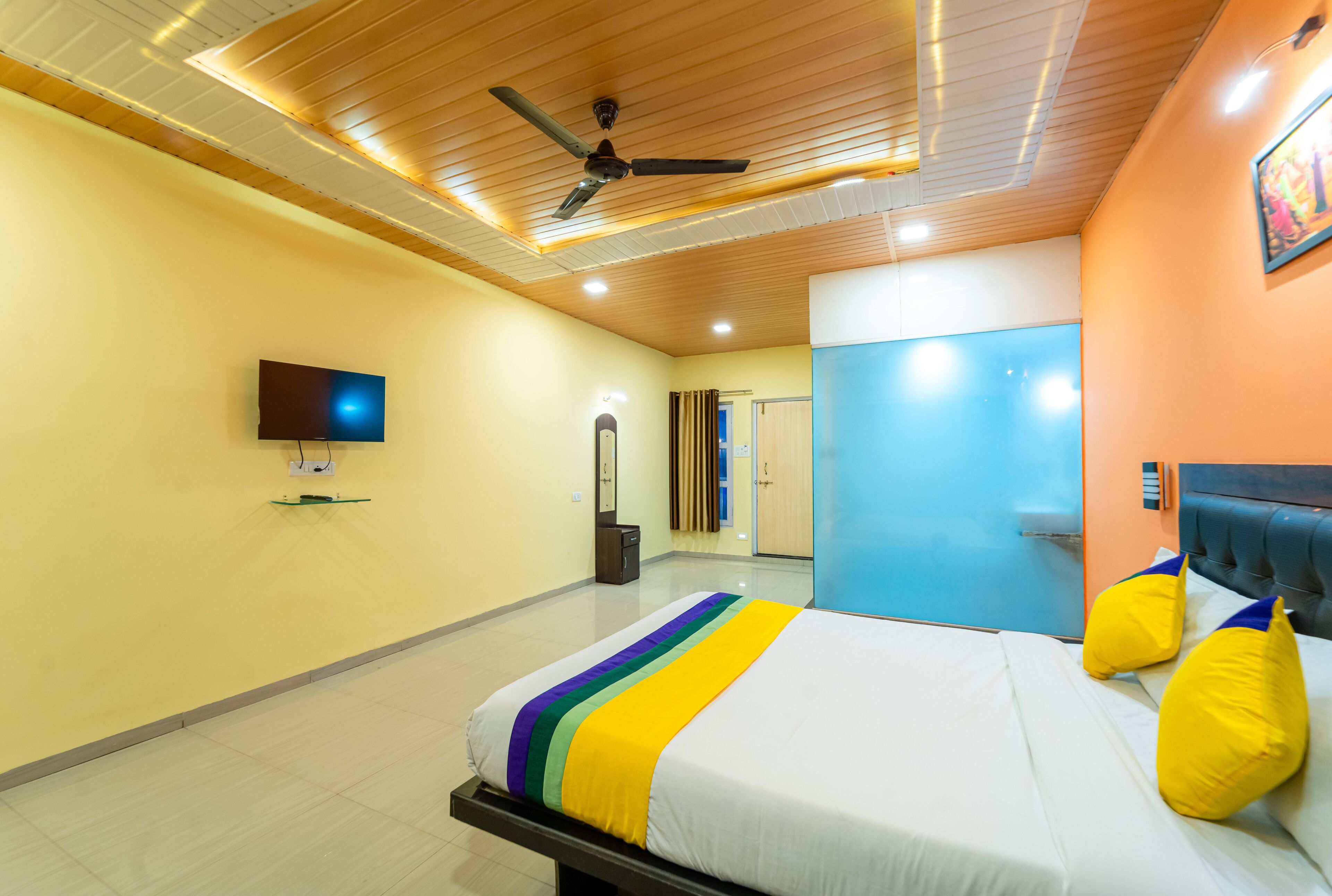 A hotel room with a bed, a ceiling fan, a television, and a bathroom door.