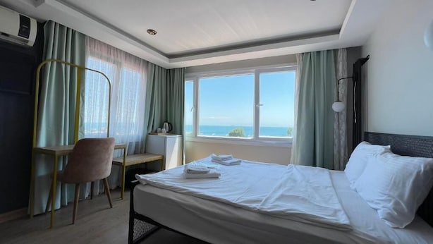 Una camera d'albergo con un letto, una scrivania e una sedia. Si vede il mare dalla finestra.