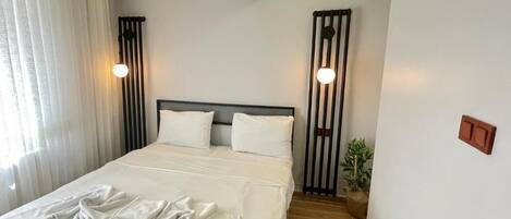 A neatly made bed with white linens, a headboard, and two wall-mounted light fixtures.