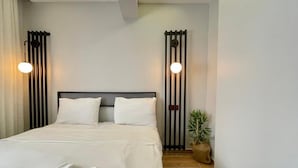 Un letto rifatto con lenzuola bianche, una testiera in metallo nero e due applique ai lati.