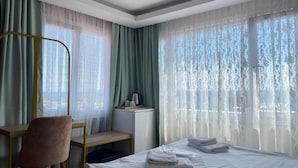Una camera d'albergo con un letto, una scrivania, una sedia, un tavolino e una finestra con tende leggere.