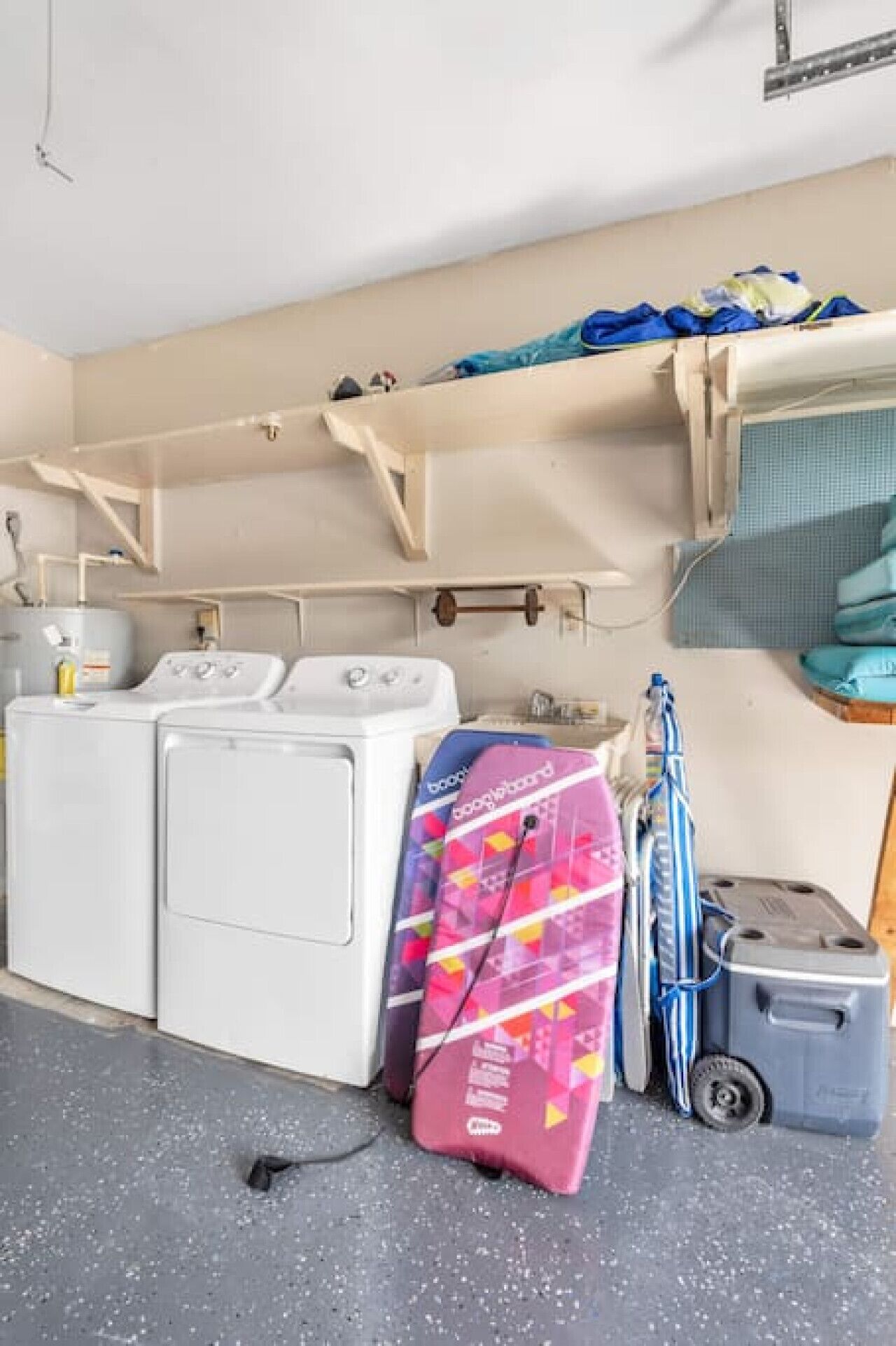 A laundry area with two white washing machines, a pink suitcase, a blue suitcase, and a gray storage bin.