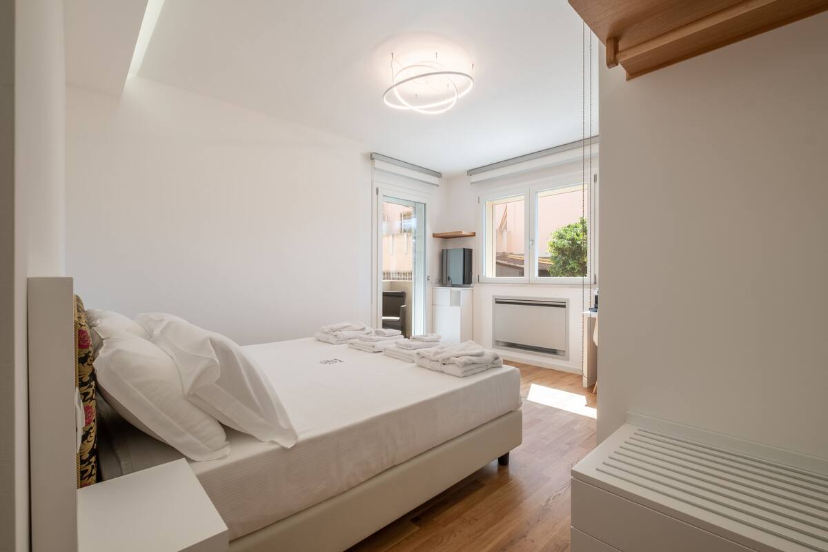 A modern bedroom with a large bed, a built-in TV, and a view of the outside through a sliding door.