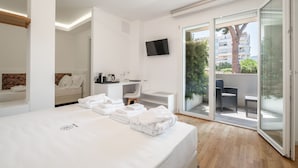 Une chambre d’hôtel moderne équipée d’un lit, d’un bureau, d’une chaise, d’une télévision et d’une porte-fenêtre coulissante donnant sur un espace extérieur.