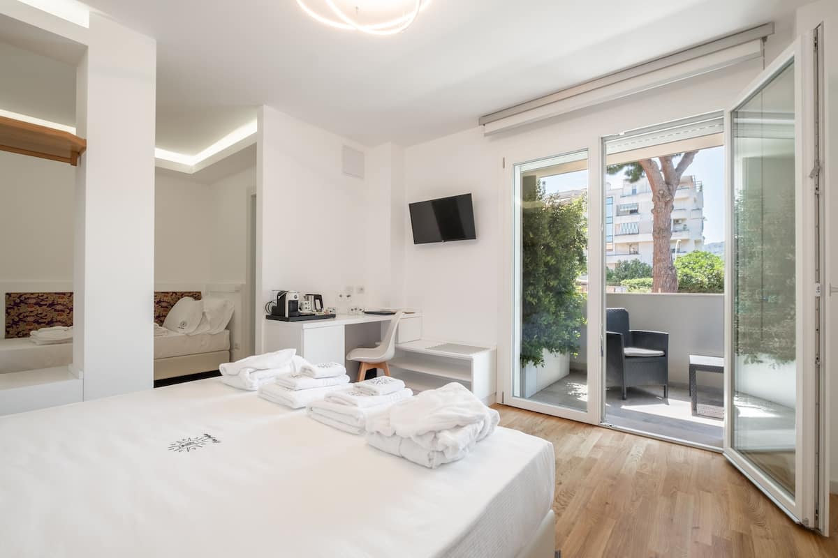 A modern hotel room with a bed, a desk, a chair, a TV, and a sliding glass door leading to an outdoor area.
