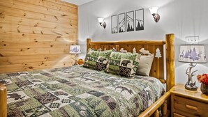 A bedroom with a wooden headboard, a quilted bedspread, and a nightstand with a lamp and a vase of flowers. - Quiet Cove 3 bdrm cabin/Smoky Mountains/Ober Gatlinburg (Gatlinburg)