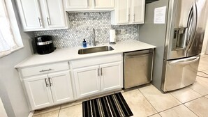 A compact kitchen with white cabinets, a stainless steel refrigerator, a coffee maker, and a sink. - FREE Heated Pool, Weber Gas Grill, 3 miles to the beach! (West Palm Beach)