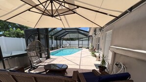 A covered patio with wicker furniture, a pool, and a glass-enclosed area. - FREE Heated Pool, Weber Gas Grill, 3 miles to the beach! (West Palm Beach)