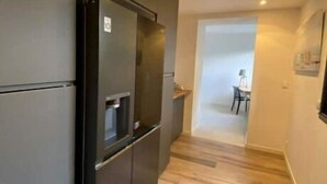 A narrow hallway with a modern kitchen area featuring a built-in black refrigerator and a water dispenser. The floor is wooden, and the walls are painted in a light color. - Villa Tixaya 5*, a cosy cocoon to recharge your batteries by the lake and ocean (Gastes)