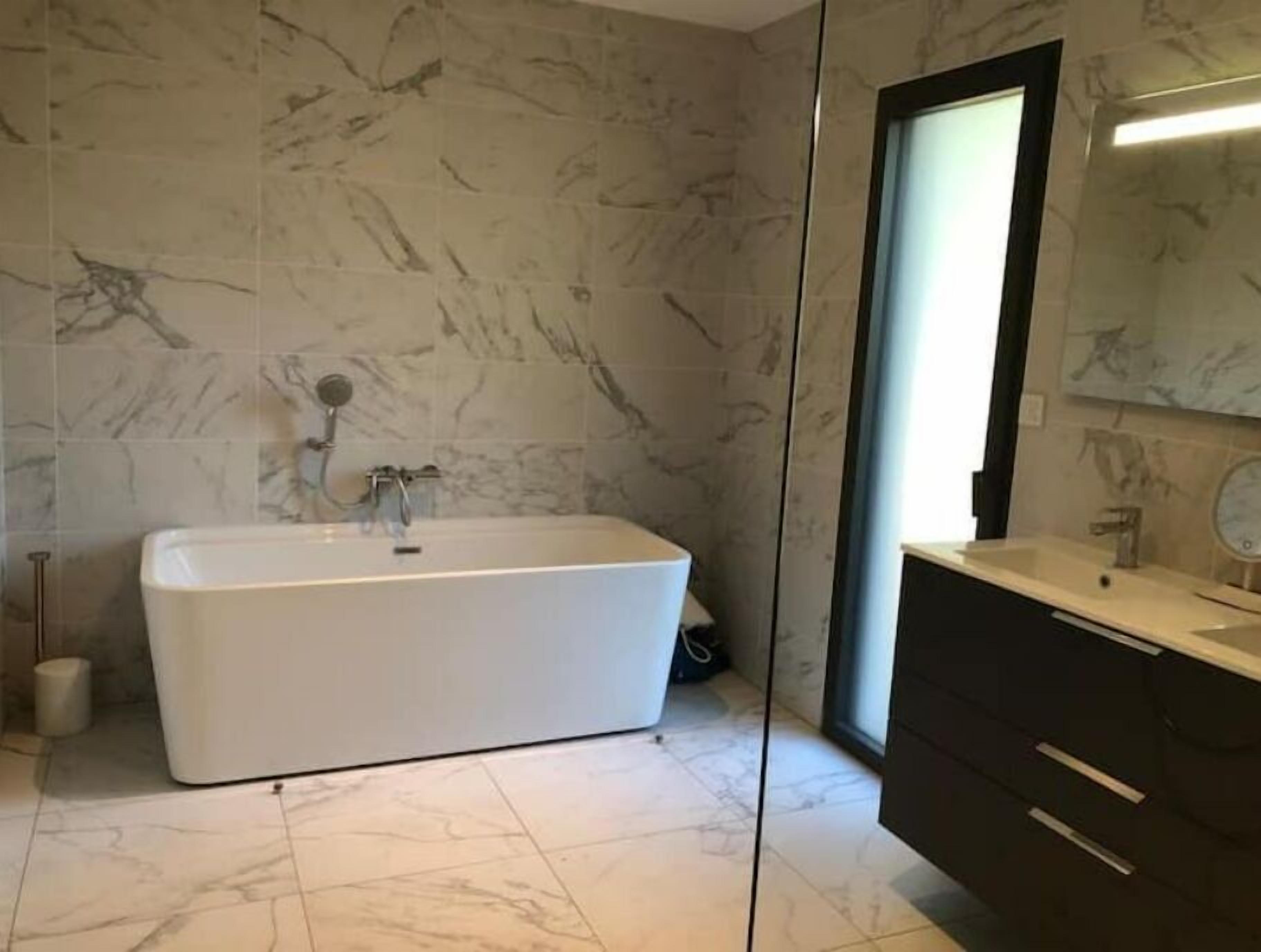 A modern bathroom with a freestanding bathtub, marble flooring, and a dark wooden vanity with a mirror.