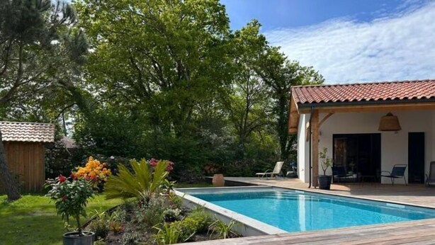 A swimming pool with a wooden deck, surrounded by lush greenery and a building with a tiled roof. - Villa Tixaya 5*, a cosy cocoon to recharge your batteries by the lake and ocean (Gastes)