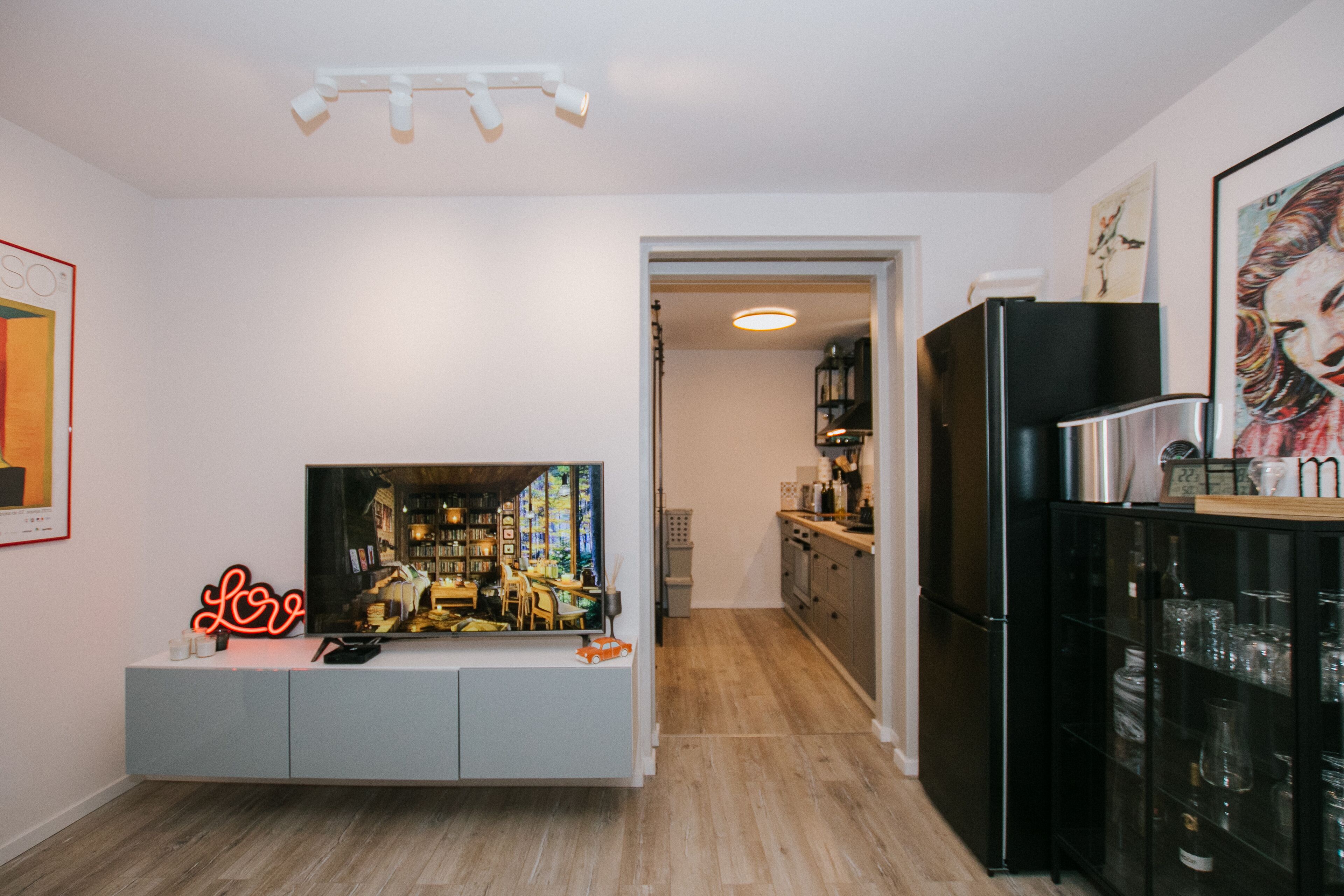 A modern kitchen with a built-in TV, a neon sign, and a black refrigerator.