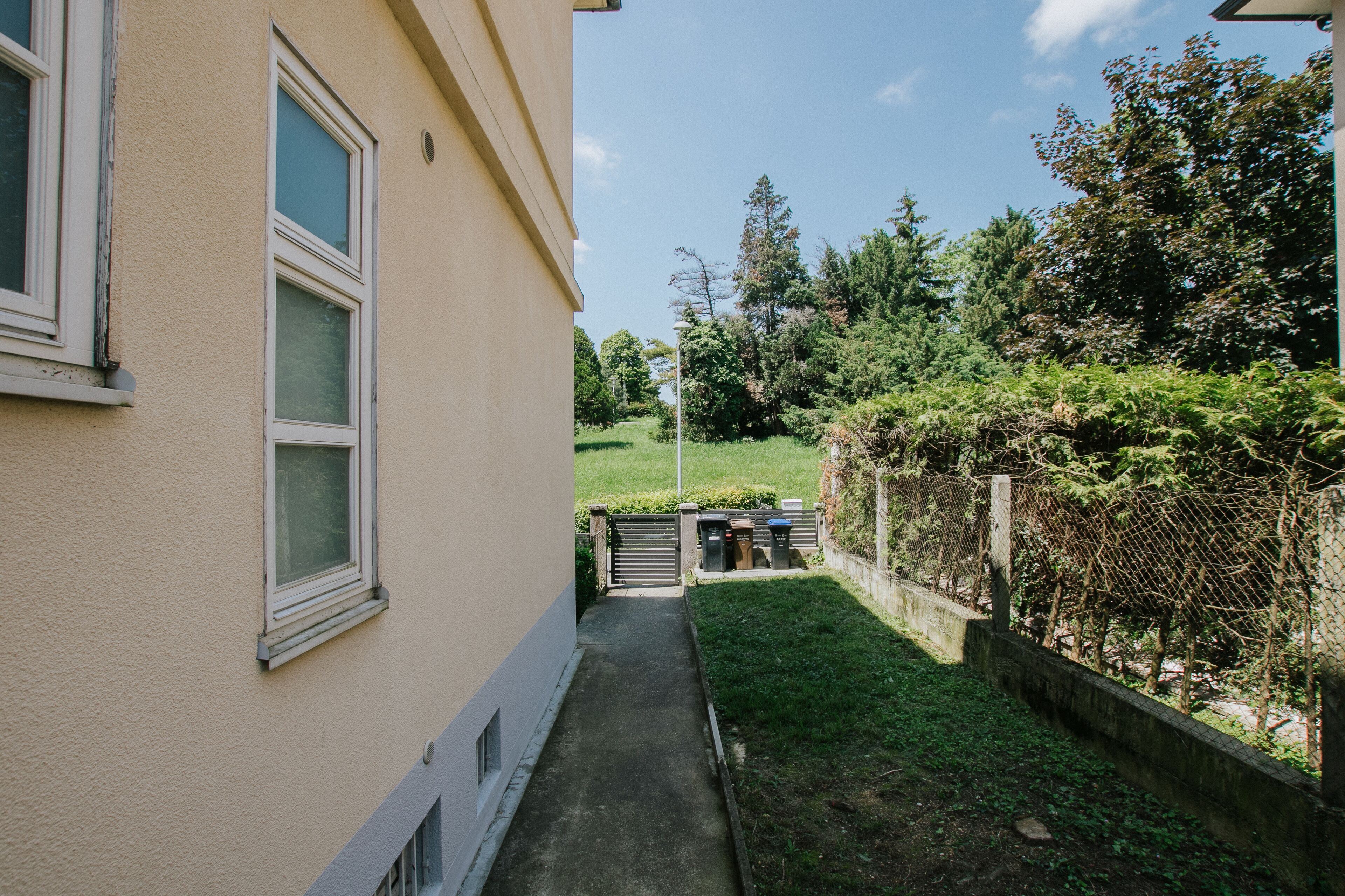A narrow pathway leading to a gated entrance with a building on one side.