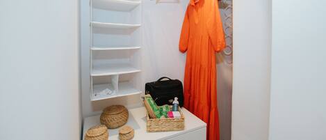 A neatly organized closet with hanging space, shelves, and a small table with baskets and a bag.