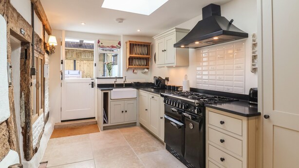 A kitchen with a skylight, white cabinets, a black stove, and a wooden shelf. - 18 Church Street (Llangollen)