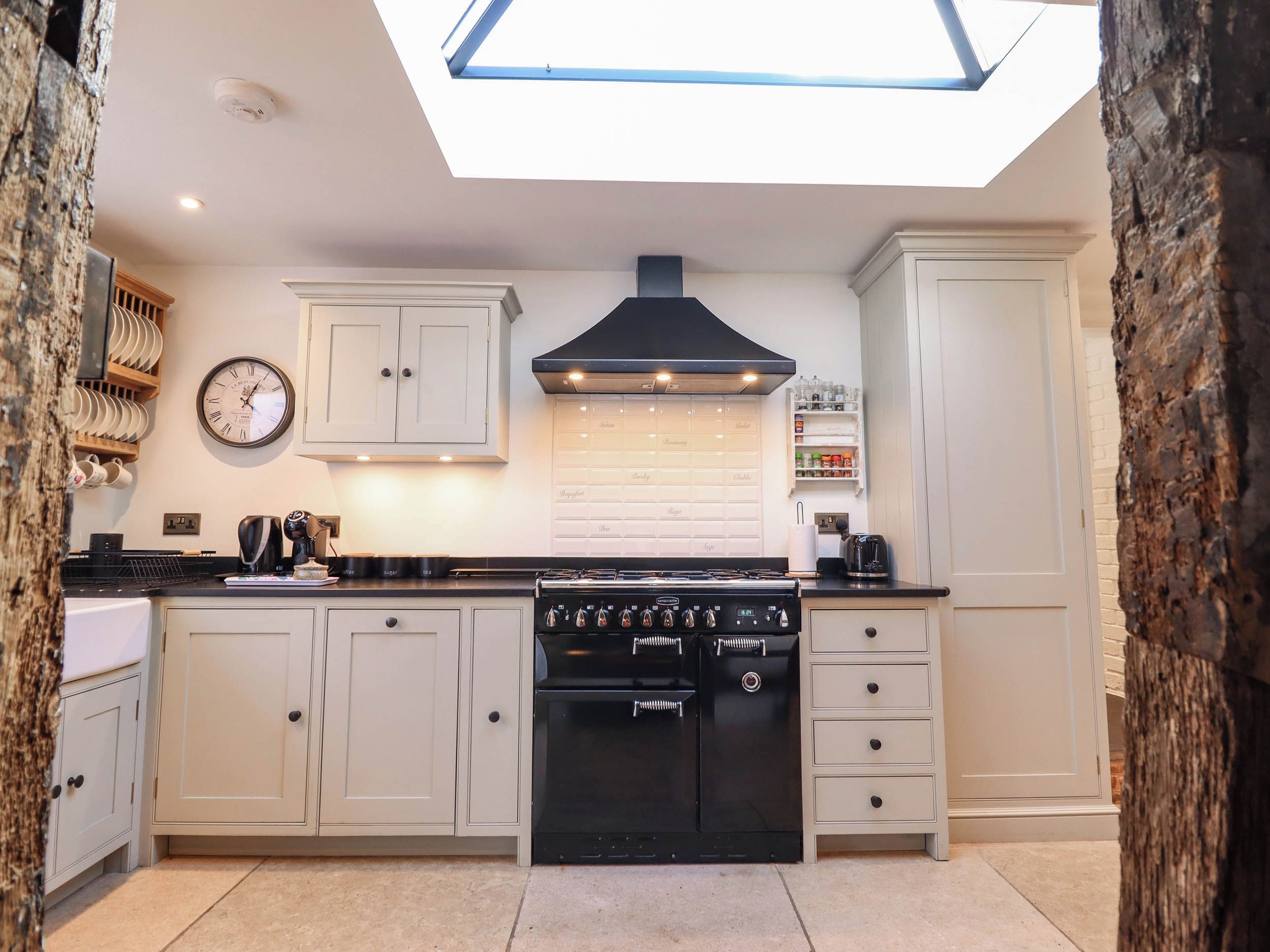 A kitchen with a skylight, white cabinets, a black stove, and a clock on the wall.