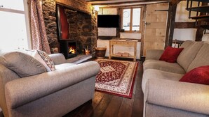 A cozy living room with a stone fireplace, two grey sofas, a red patterned rug, and wooden beams on the ceiling. - 18 Church Street (Llangollen)