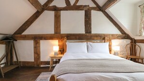 A bedroom with a wooden ceiling, a bed with white linens, two bedside tables with lamps, and a chair. - 18 Church Street (Llangollen)