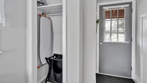 Un pasillo con una puerta, una ventana con persianas y un cesto de ropa.