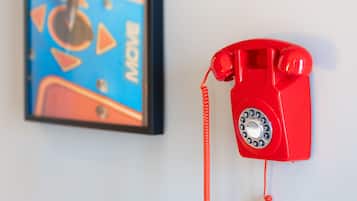 A red rotary phone mounted on a white wall next to a framed abstract painting.
