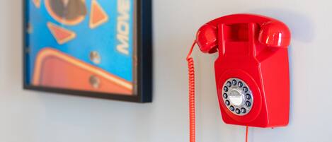 A red rotary phone mounted on a white wall next to a framed abstract painting.