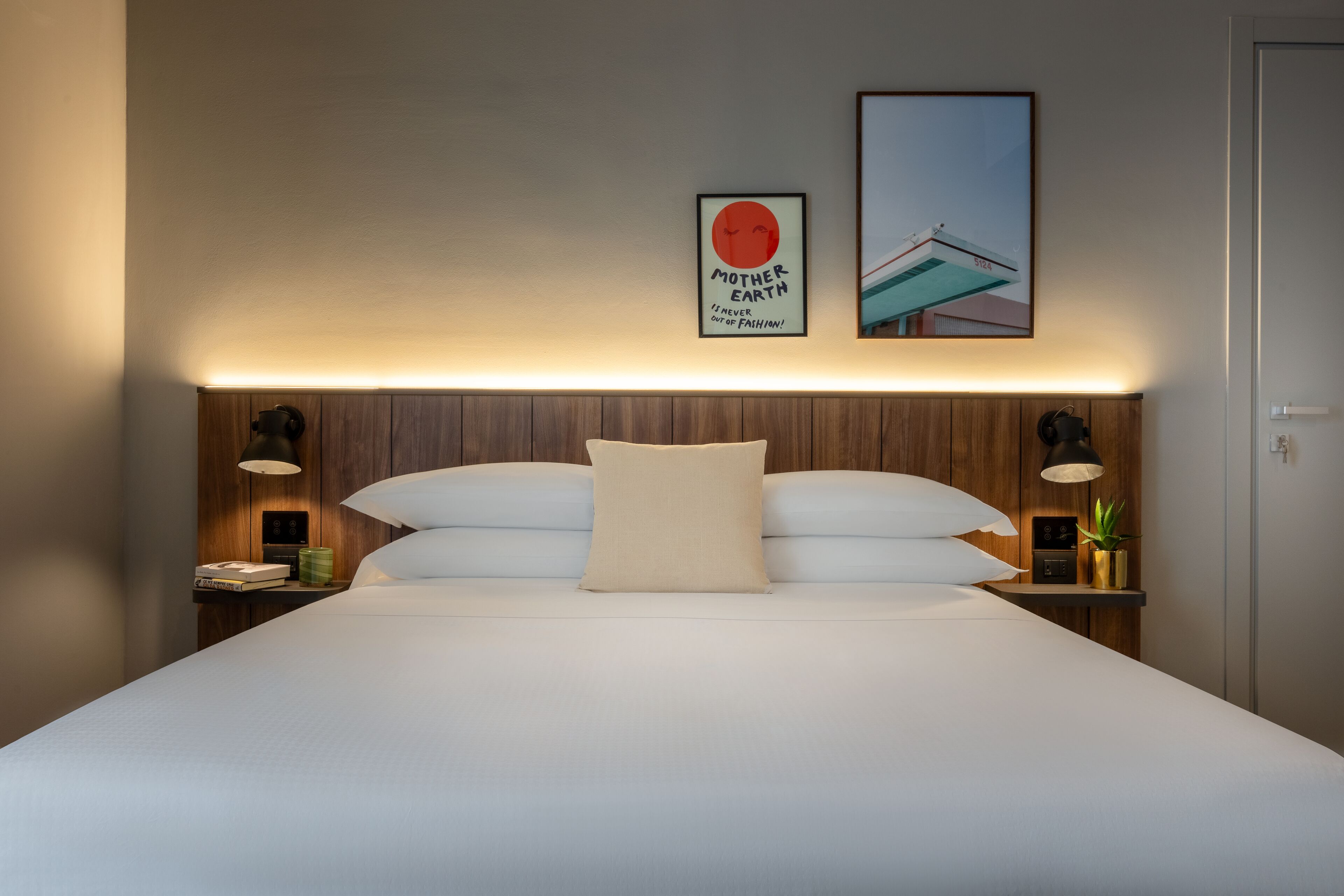 A neatly made bed with a headboard, two bedside tables with lamps, and two framed pictures on the wall.