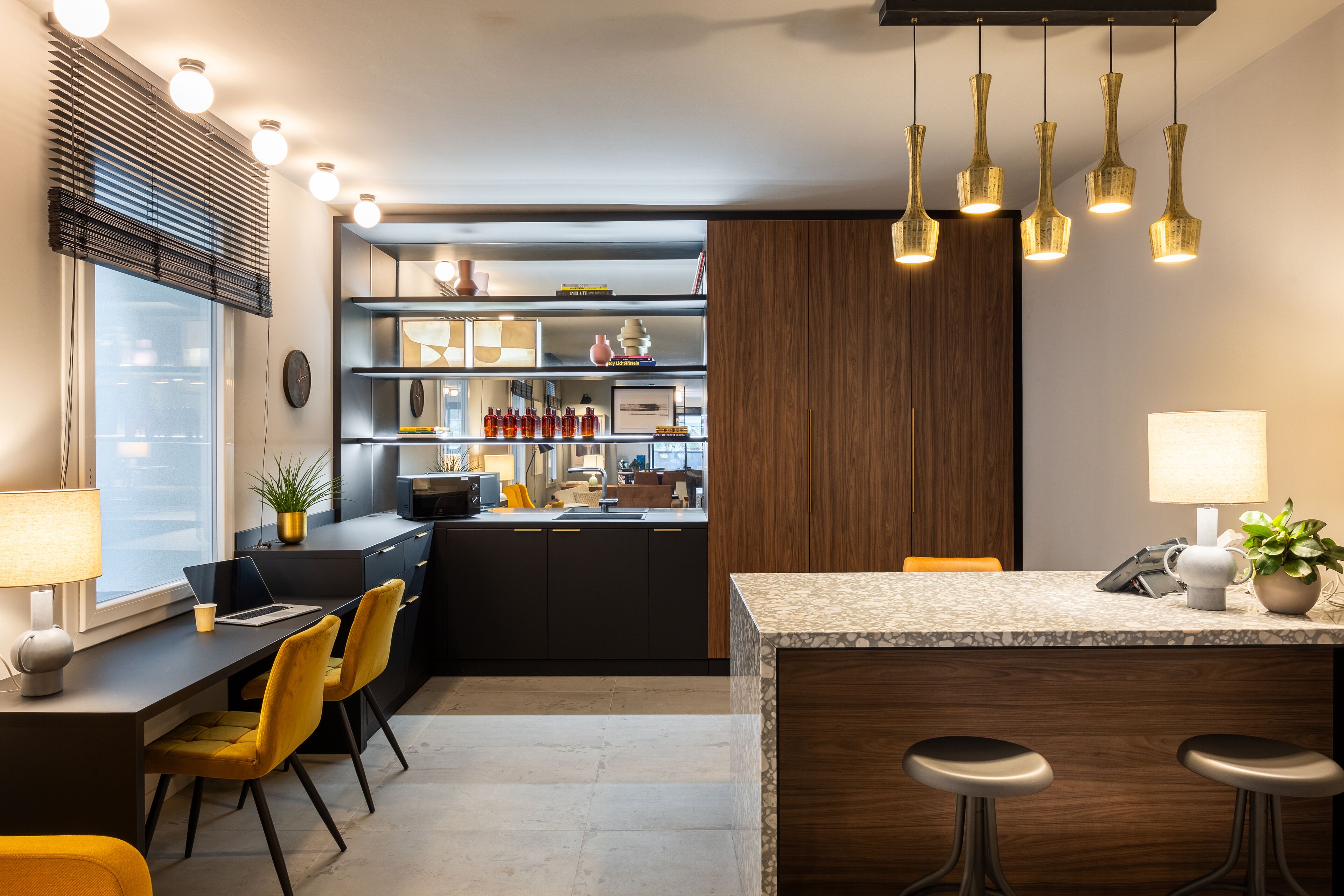 Una cocina moderna con una isla central, taburetes de bar y un comedor con una silla amarilla.