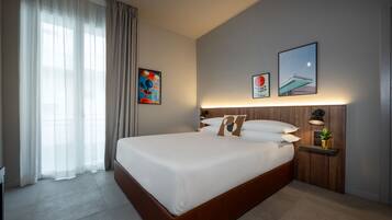 Una habitación de hotel moderna con una cama grande, una mesita de noche con lámpara y obras de arte en las paredes.