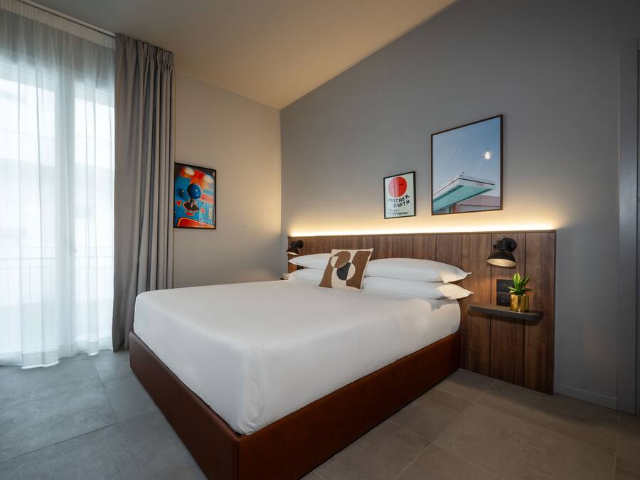 Ein modernes Hotelzimmer mit einem großen Bett, einem Nachttisch mit Lampe und Bildern an den Wänden.