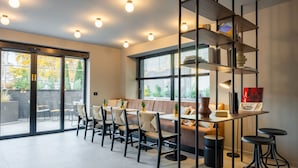 Un café moderno con una barra larga, varias mesas y sillas. También hay un sofá y una estantería con distintos objetos.