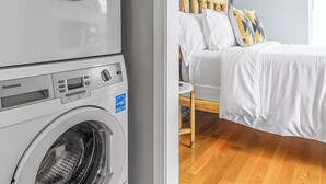 A laundry area with a front-loading washer and dryer, a bed with white bedding, and a wooden headboard. - Cozy Queen, Private Bathroom and Entryway (Bend)