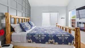 A bedroom with a wooden headboard, a patterned bedspread, a white mattress, and a bedside table with a remote control. - Cozy Queen, Private Bathroom and Entryway (Bend)