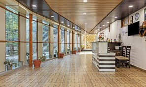 A spacious lobby with large windows, wooden flooring, a reception desk, and a stone wall in the background. - Treebo Olive Lake View Inn June Estate Bhimtal (Nainital)