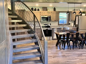 A modern kitchen with a wooden staircase, stainless steel appliances, and a dining area with black chairs. - Trophy Trout Fishing on Property and 1 mi to VC Park (Sugar Grove)