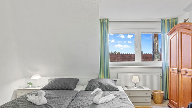 Une chambre à coucher comprenant un lit, des tables de chevet, une commode, une fenêtre avec des rideaux et une armoire.