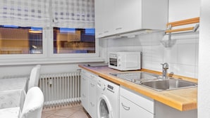Une cuisine compacte équipée d’un lave-linge, d’un four à micro-ondes et d’un évier.