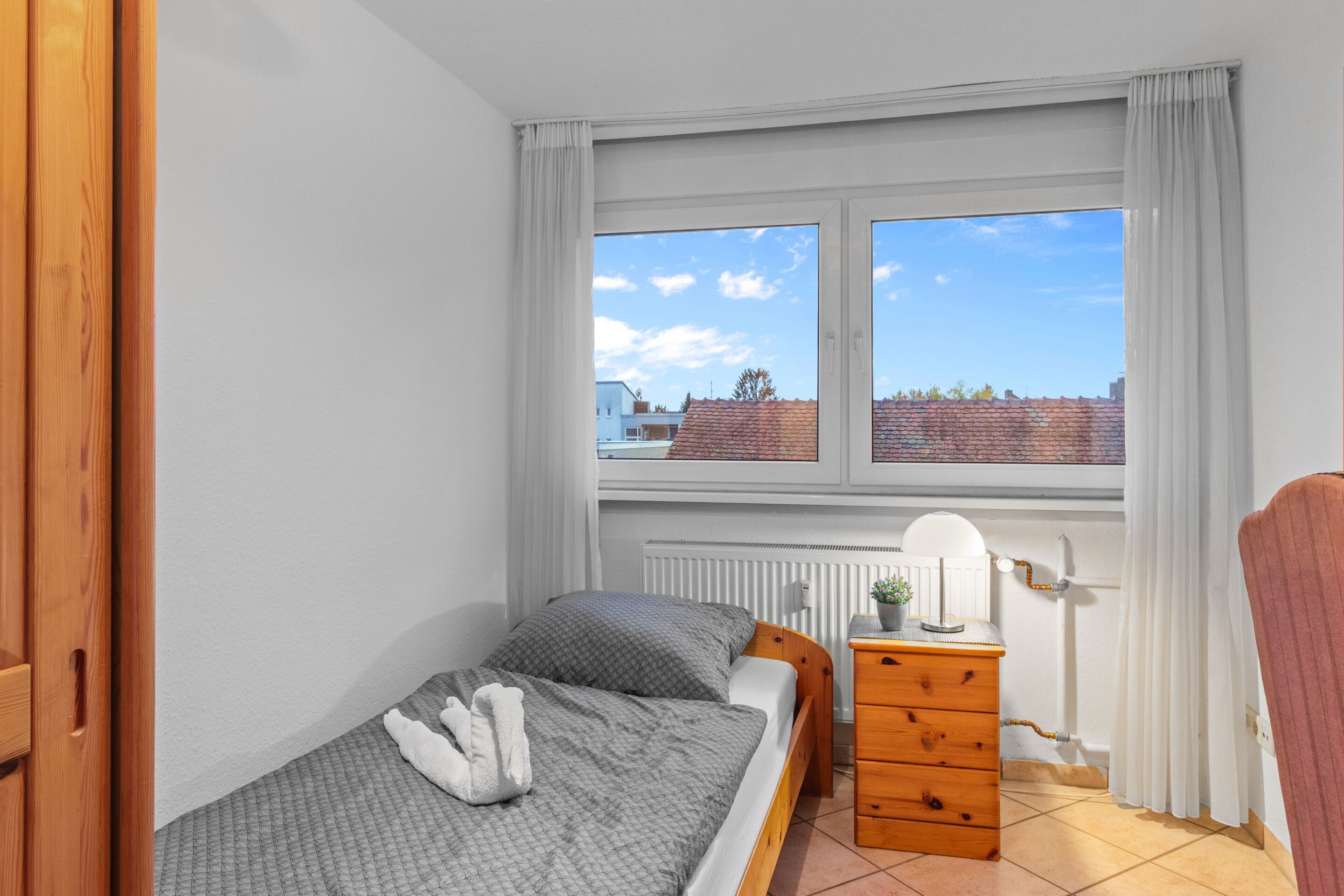 A bedroom with a bed, a dresser, a radiator, and a window with curtains.