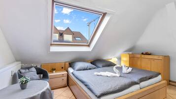A bedroom with a skylight, a bed with a grey bedspread, a bedside table with a plant, and a wooden wardrobe.