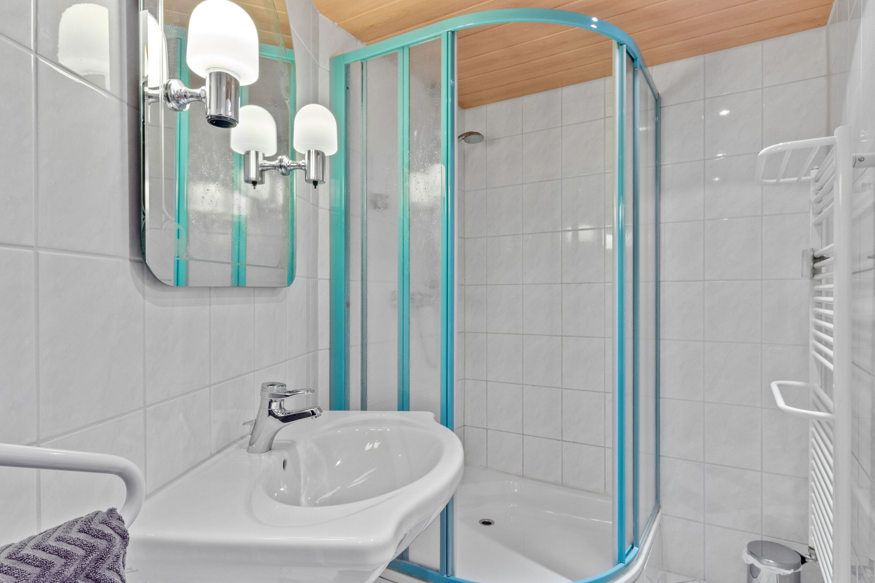 A modern bathroom with a glass shower enclosure, a white sink, and a mirror with lights.