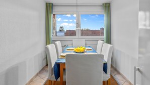 Un coin repas avec une table dressée pour quatre personnes, une fenêtre avec des rideaux et une vue sur les bâtiments à l’extérieur.