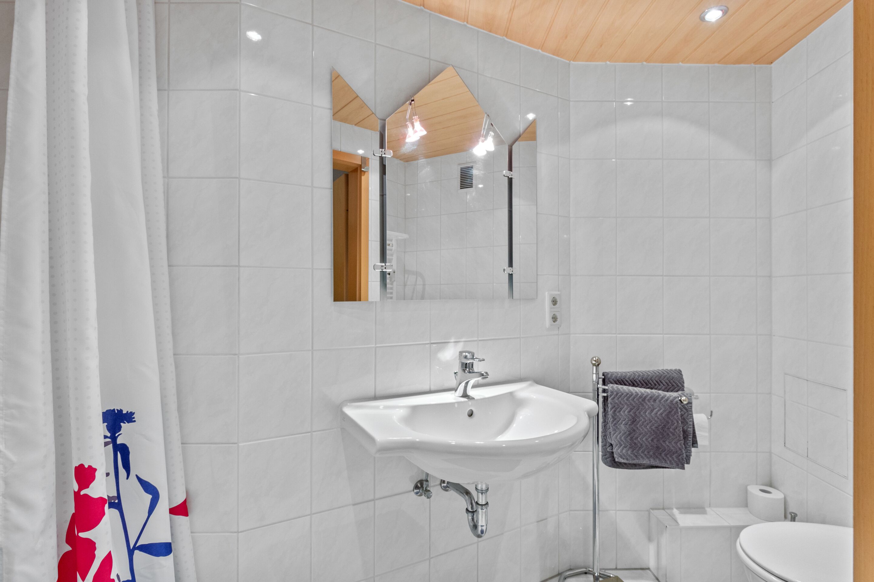 A modern bathroom with a white sink, mirror, and toilet.