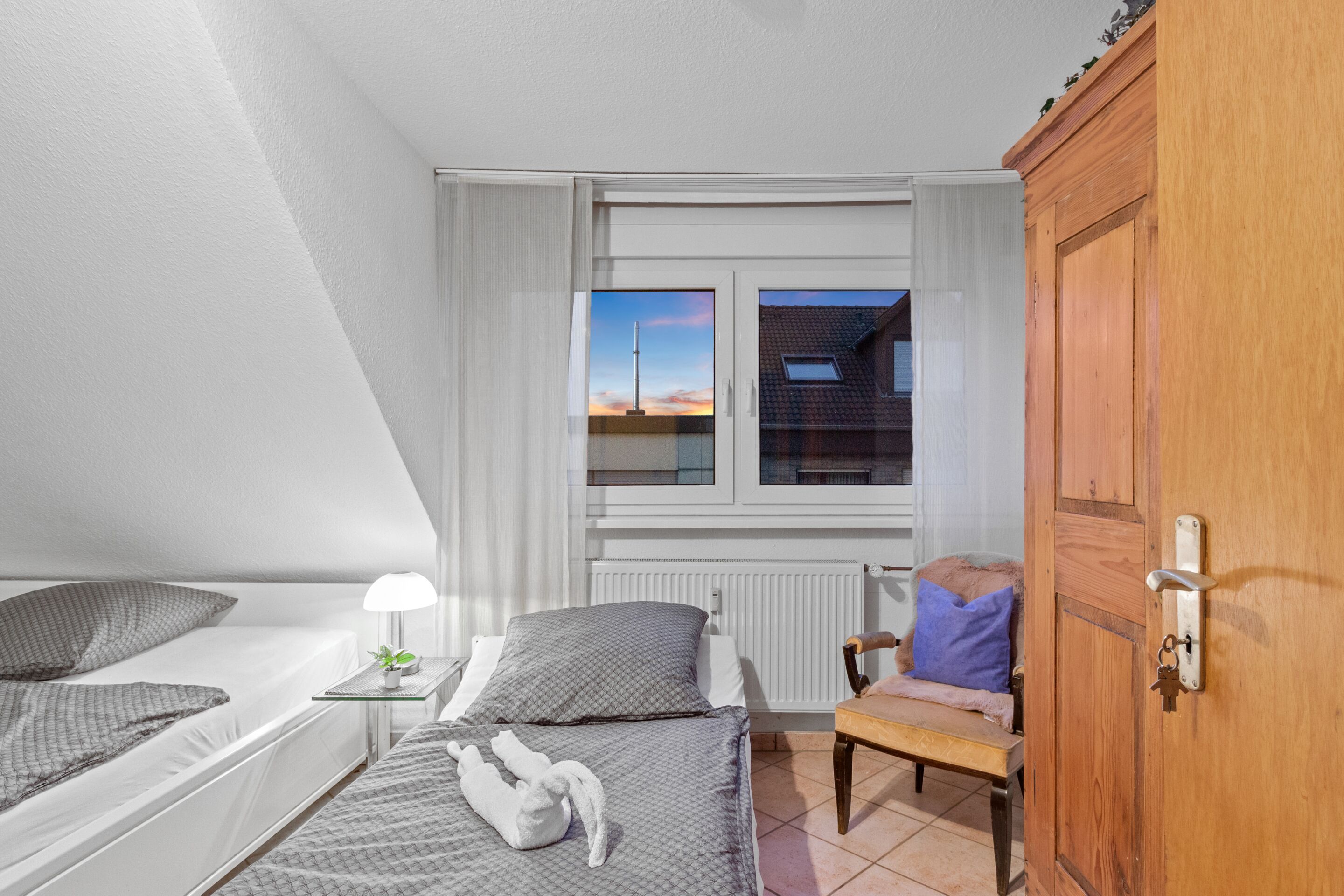 Une chambre avec deux lits, une fenêtre donnant sur un beau paysage, une armoire en bois et une table de chevet avec une lampe.