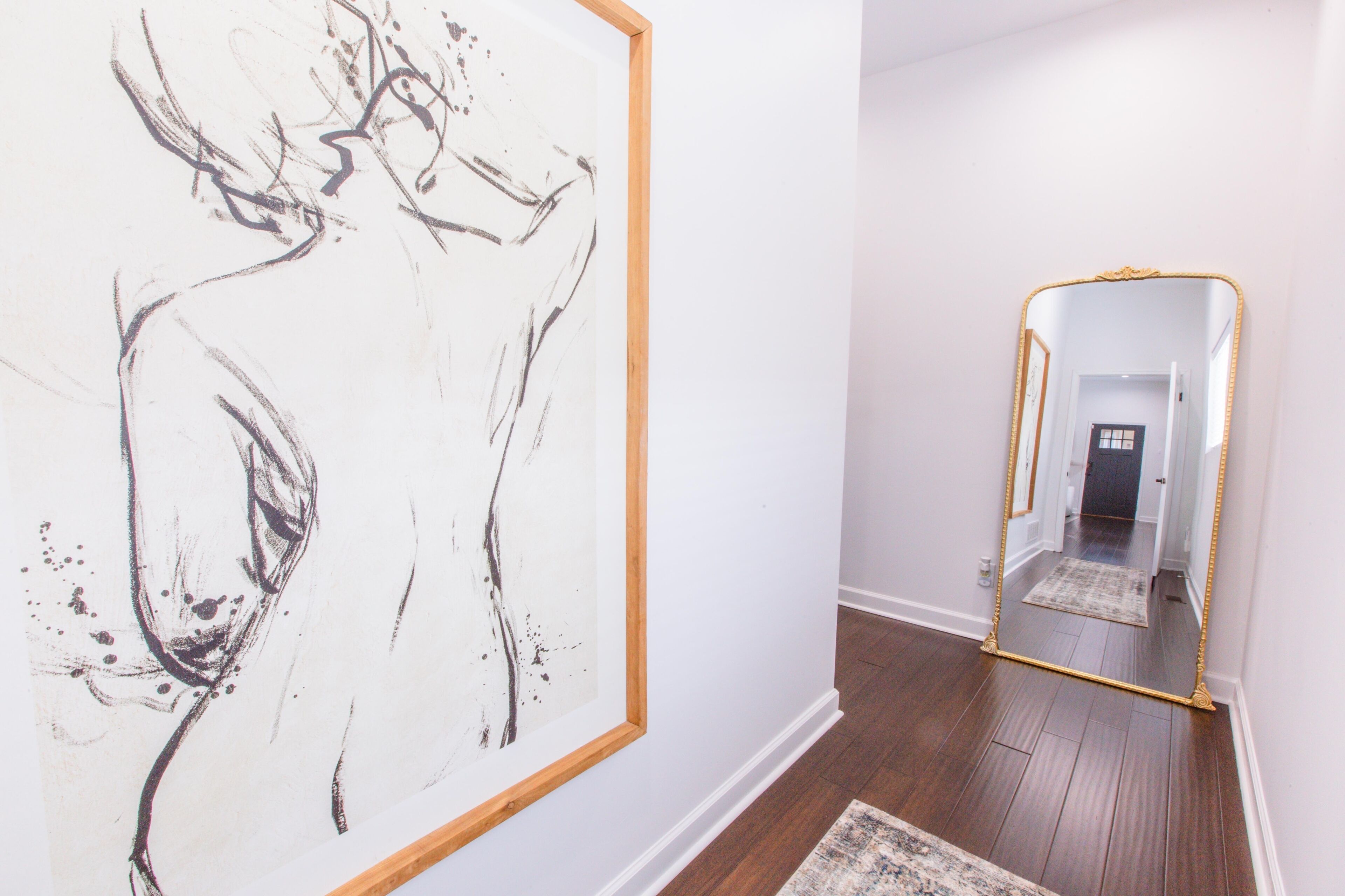 Un couloir avec une grande peinture abstraite sur le mur de gauche et un miroir avec un cadre doré sur le mur de droite.