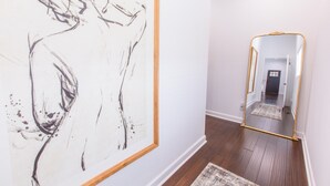 A hallway with a large abstract painting on the left and a mirror with a gold frame on the right. - Chic & Cozy Home Near UK Campus! Perfect for Family Visits. (Lexington)