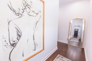 Un corridoio con un grande dipinto astratto sul lato sinistro e uno specchio con cornice dorata a destra.