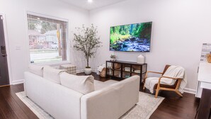 A living room with a sofa, a wooden chair, a TV, and a plant. - Chic & Cozy Home Near UK Campus! Perfect for Family Visits. (Lexington)